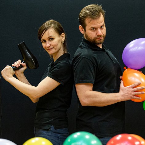 Dwoje animatorów w czarnych koszulkach z kolorowymi balonami