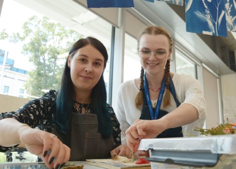  Dwie kobiety w fartuchach uśmiechają się, pracując wspólnie nad projektem plastycznym.