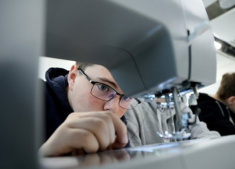  Chłopak w okularach z dużym skupieniem nawleka nić w maszynie do szycia.