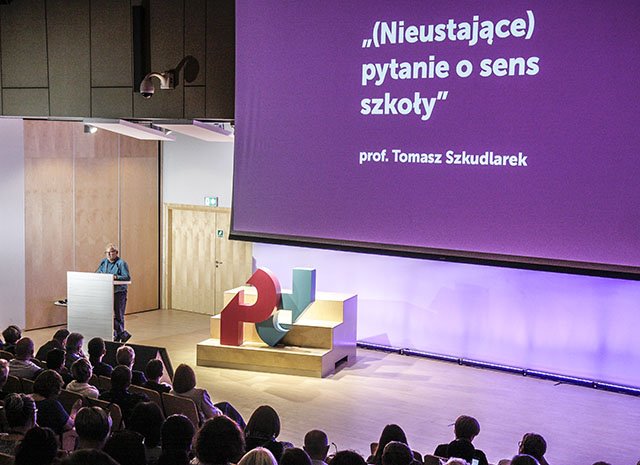 Widok sceny w czasie konferencji, na rozwiniętym rzutniki fioletowy slajd z hasłem "Pytanie o sens szkoły"