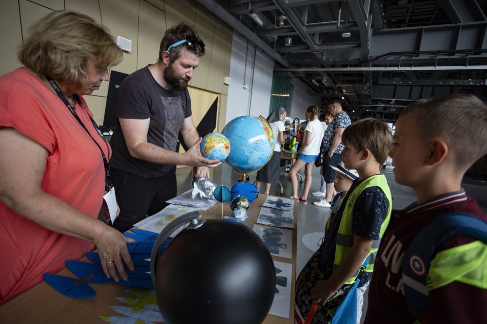 Stoisko z globusami, przy którym dwoje dorosłych tłumaczy coś dzieciom.