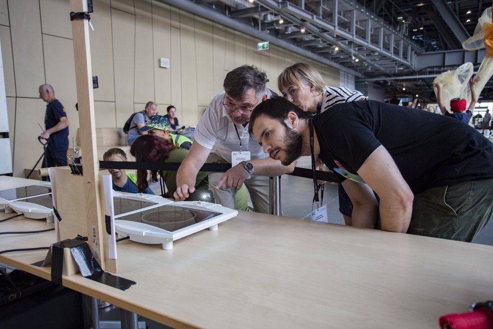 troje dorosłych przyglądających się prototypowi eksponatu.