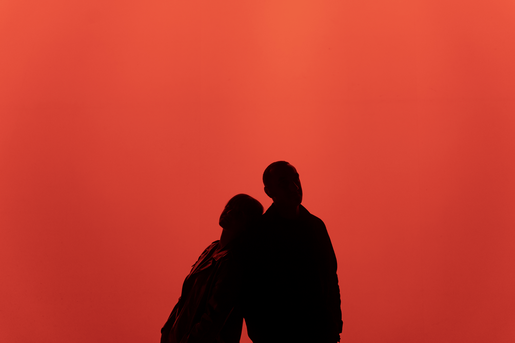 dwoje artystów opartych o siebie na czerwonym tle