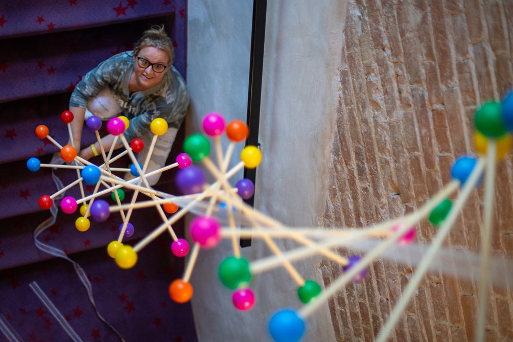 Na zdjęciu widać kobietę siedzącą na schodach i spoglądającą w górę na falodrom skonstruowany podczas Szkoły Prototypowania.