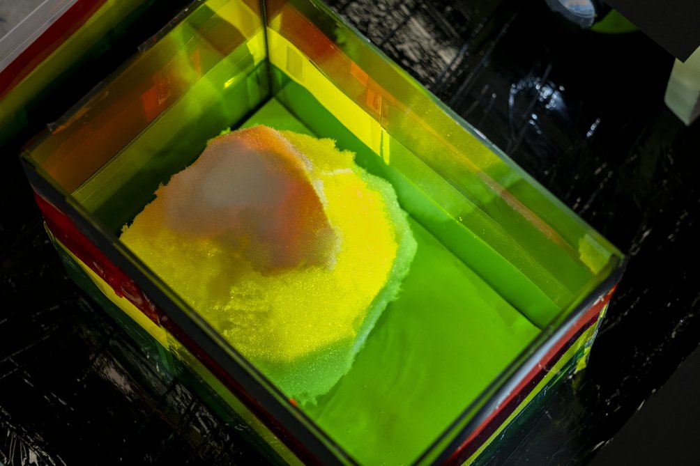 Zdjęcie przedstawia interaktywny eksponat, który umożliwia tworzenie trójwymiarowej mapy topograficznej z piasku. Kolory podświetlenia zmieniają się w zależności od wysokości terenu, symulując różnicę wysokości na mapach hipsometrycznych.