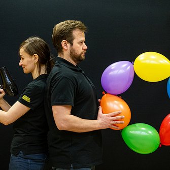 Dwoje animatorów w czarnych koszulkach z kolorowymi balonami