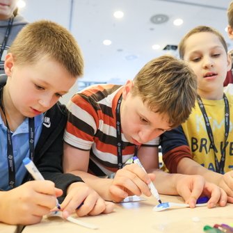 Grupa dzieci przy stole, piszą kolorywmi mazakami na kartkach