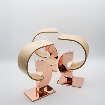 Trzy statuetki „Przewroty” ustawione razem, ukazujące detal formy i połyskującego materiału.