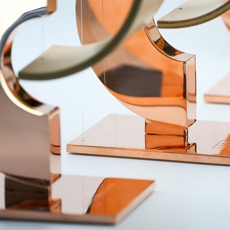 Detal podstawy statuetek „Przewroty” z wyraźnie widocznym napisem oraz odbiciem łukowej formy.