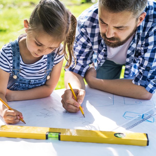 Ojciec i córka rysują w plenerze przy stole, na dużym arkuszu białego papieru rysunek techniczny  