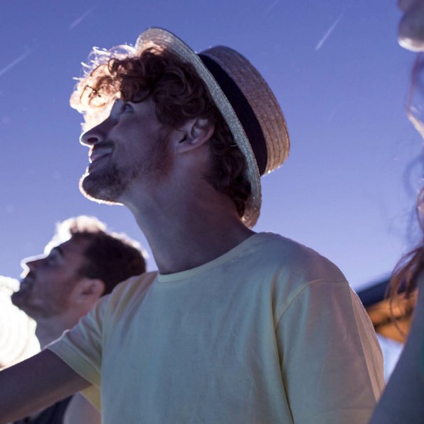 Troje ludzi w letnich strojach wpatrzonych w nocne niebo, na którym widać spadające gwiazdy.