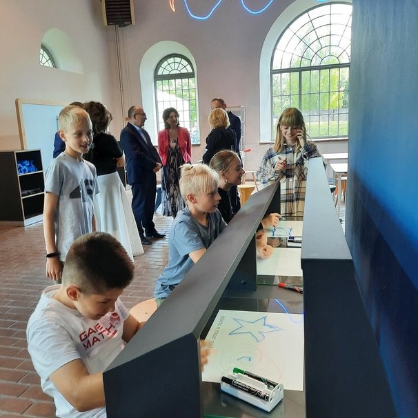 Uśmiechnięte dzieci eksperymentują przy eksponacie Rysowanie w lustrze na wystawie w nowo otwartej  strefie SOWA w Starachowicach.
