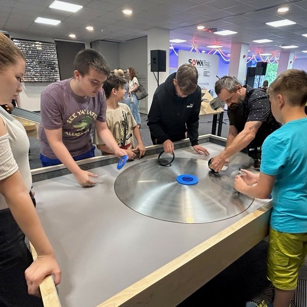  Młodzież eksperymentuje wspólnie z nauczycielem przy eksponacie „Obrotowy stolik”.