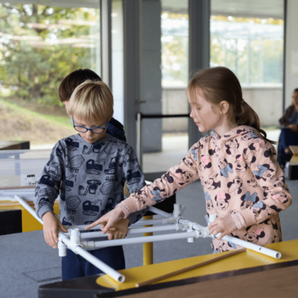 Dwoje dzieci konstruuje most z białych rurek