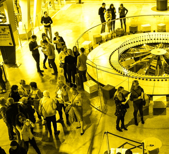 Zdjęcie w żółto-czarnych barwach, widok z góry na ludzi wokół eksponatu.