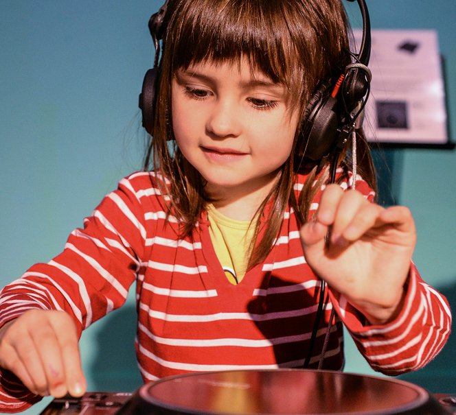 Dziewczynka w słuchawkach na uszach, kręci przyciskami jak a konsolecie muzycznej.
