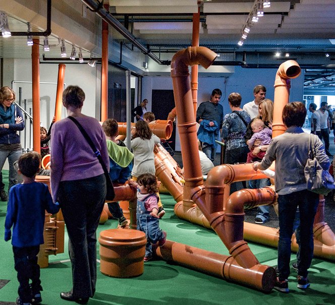 Widoczna przestrzeń wystawy, konstrukcja z ogromnych rur wokół której krążą dorośli i dzieci.
