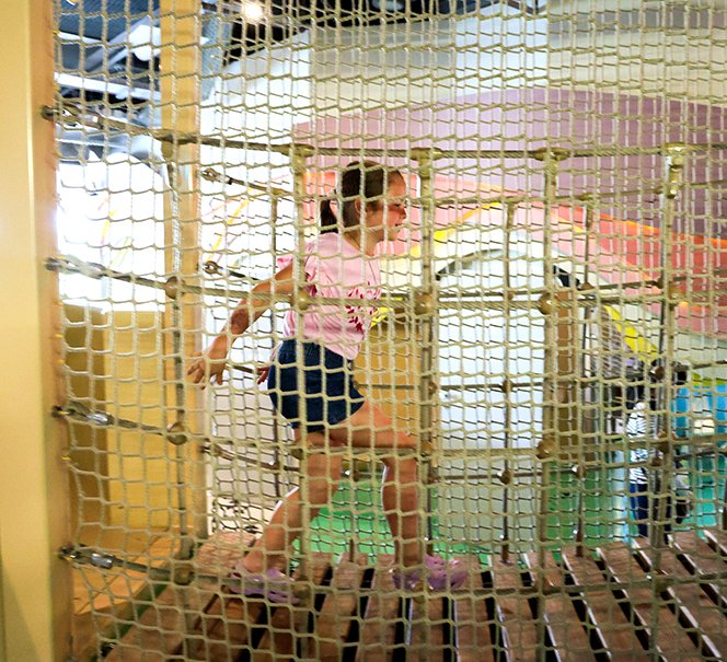 Dziewczynka przechodzi przez linowy tunel wspinaczkowy na wystawie.