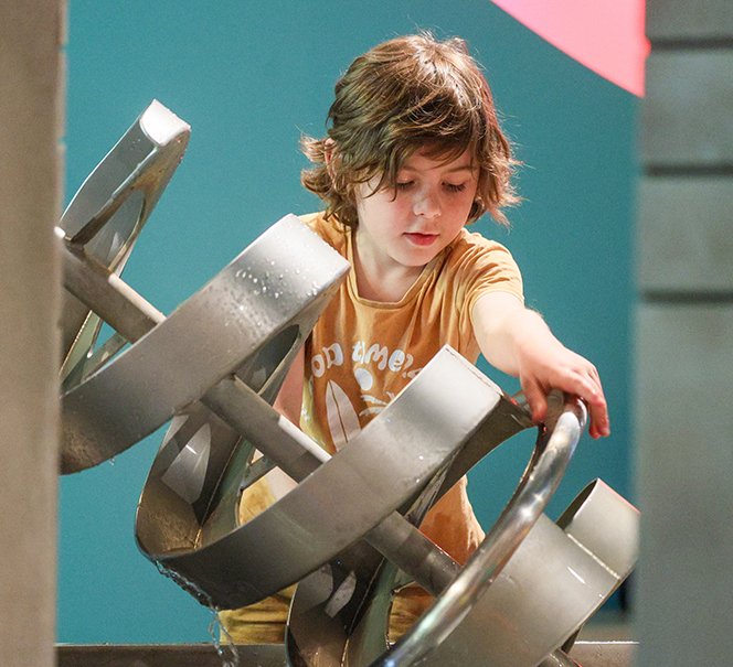 Chłopiec obraca śrubę Archimedesa w interaktywnej instalacji wodnej.