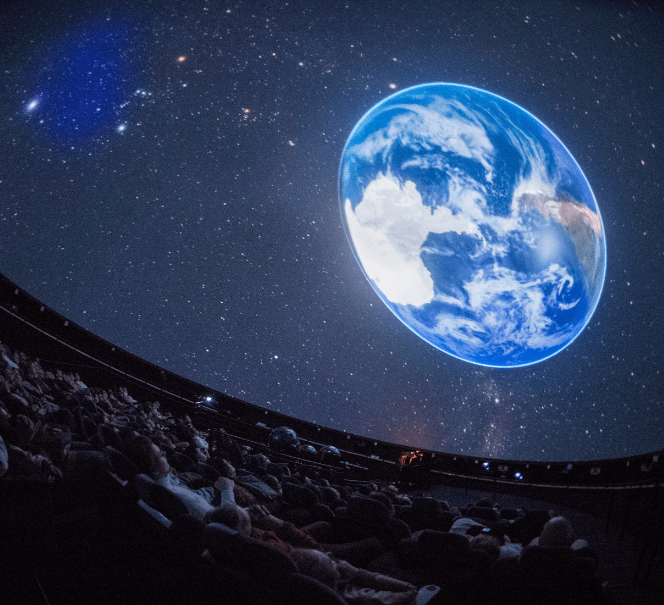 Publiczność w planetarium ogląda realistyczną projekcję planety Ziemia na kopule nad głowami.