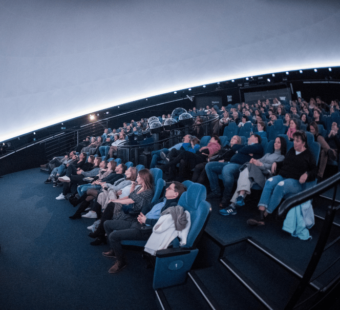 Sala planetarium wypełniona widzami siedzącymi w rzędach, patrzącymi w stronę kopuły.