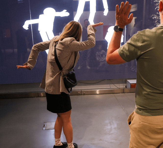 Dwie osoby wchodzą w interakcję z ekranem, na którym pojawiają się ich cienie.