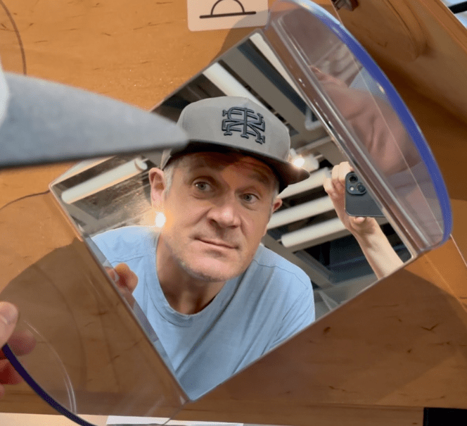 Mężczyzna zagląda w lustro w eksperymencie optycznym, odbicie pokazuje jego twarz z różnych perspektyw.