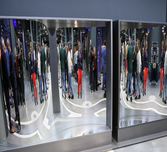 Grupa ludzi stoi przed dużymi lustrami zniekształcającymi sylwetki.