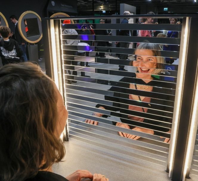 Dwie osoby siedzą naprzeciw siebie przy instalacji z poziomymi paskami i światłami.