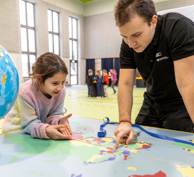 Dziecko i dorosły człowiek nad mapą, pokazują coś sobie.