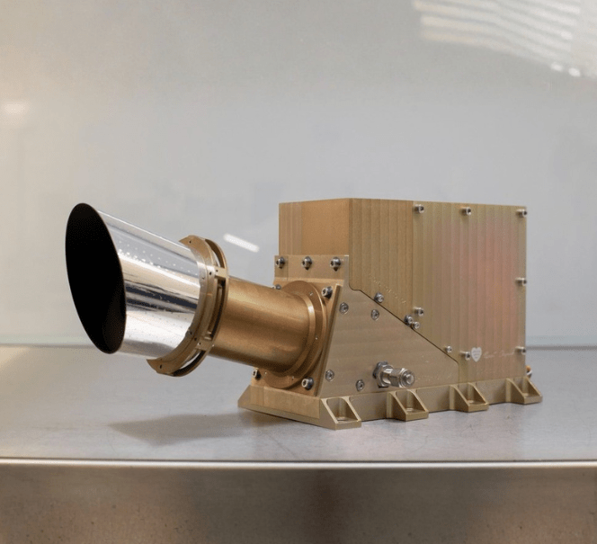 Złoty instrument naukowy z cylindrycznym wlotem umieszczony na stole – element aparatury do badań kosmicznych lub pomiarów.