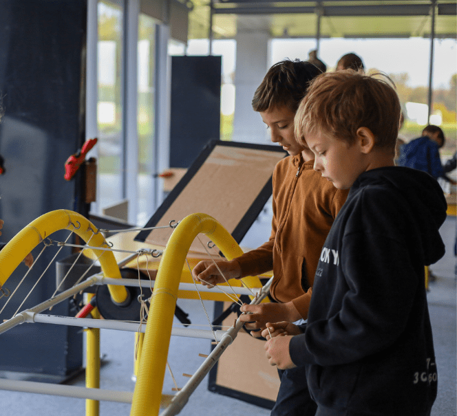 Dwóch chłopców pracuje przy stanowisku konstrukcyjnym, łącząc elementy i przewody w ramach zadania technicznego.